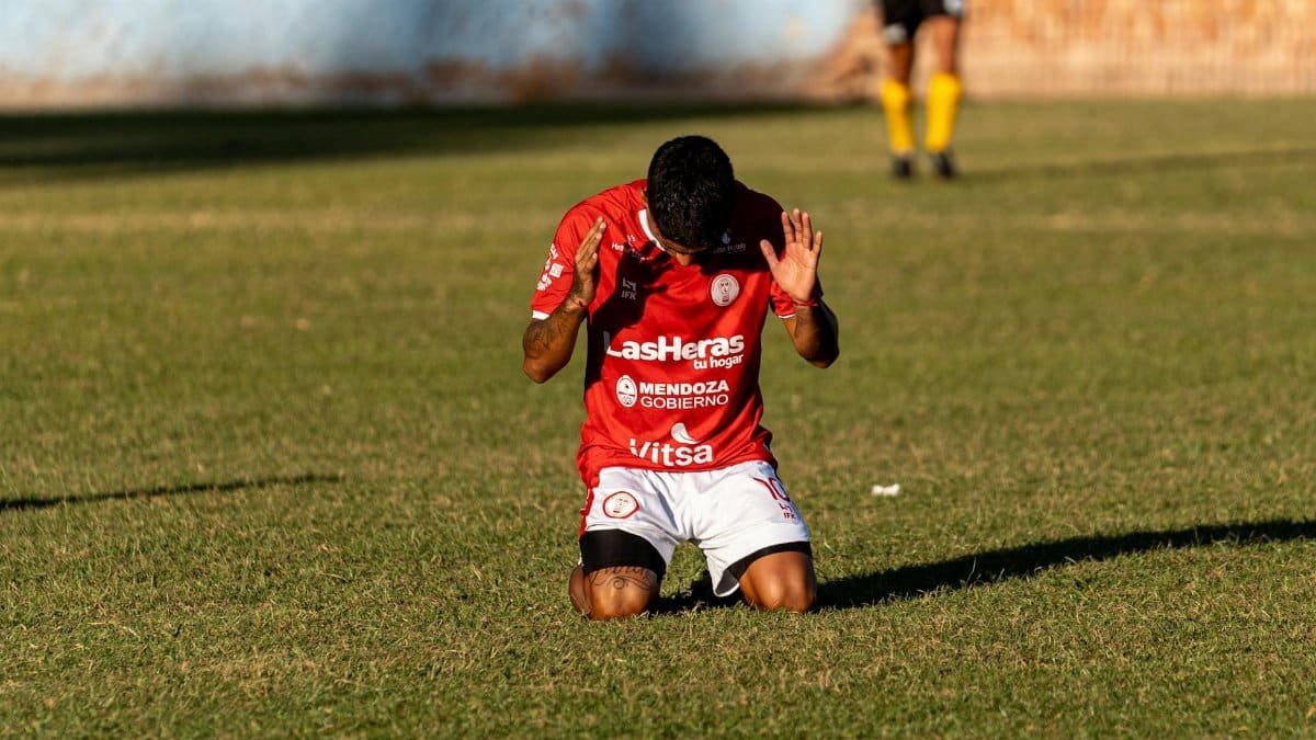 Soccer player kneeling on field expressing gratitude or prayer during a match.