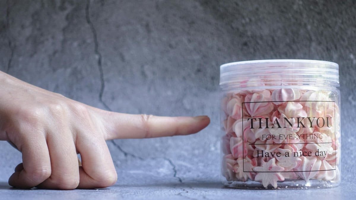 A hand points at a jar filled with pink meringue cookies displaying a thank you message.