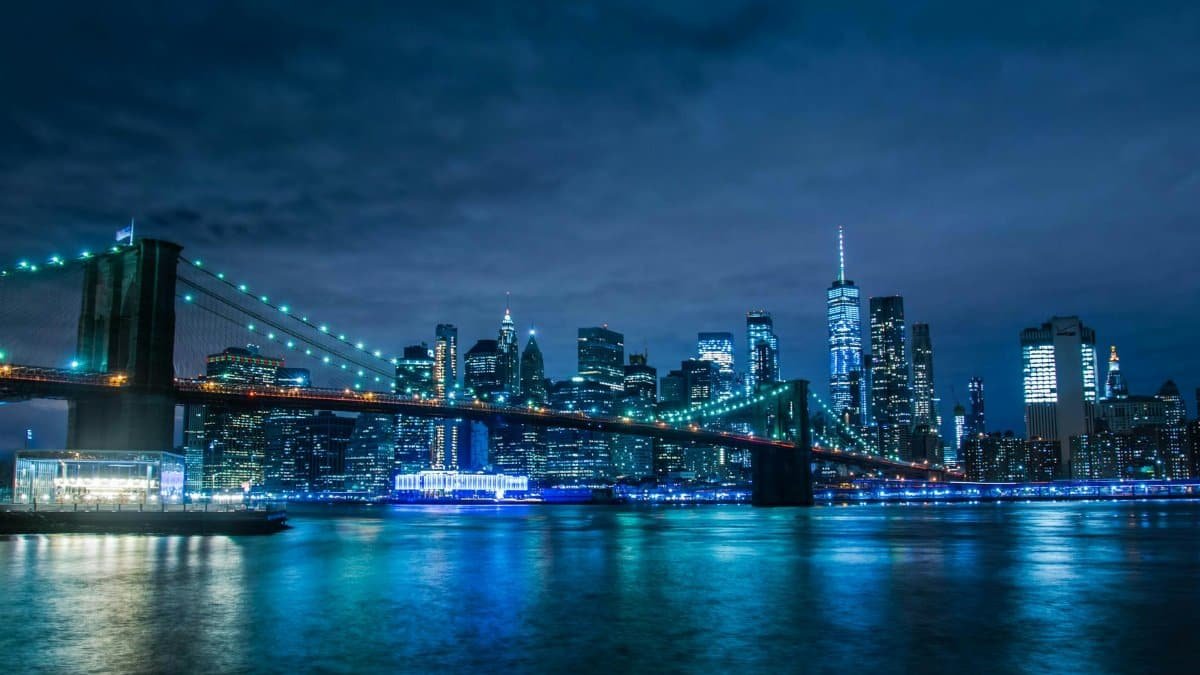 Stunning night view of the illuminated Brooklyn Bridge and New York City skyline across the water.