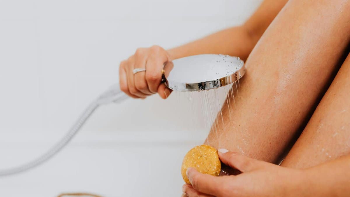 Close-up of hands holding soap and shower head, highlighting skincare routine.