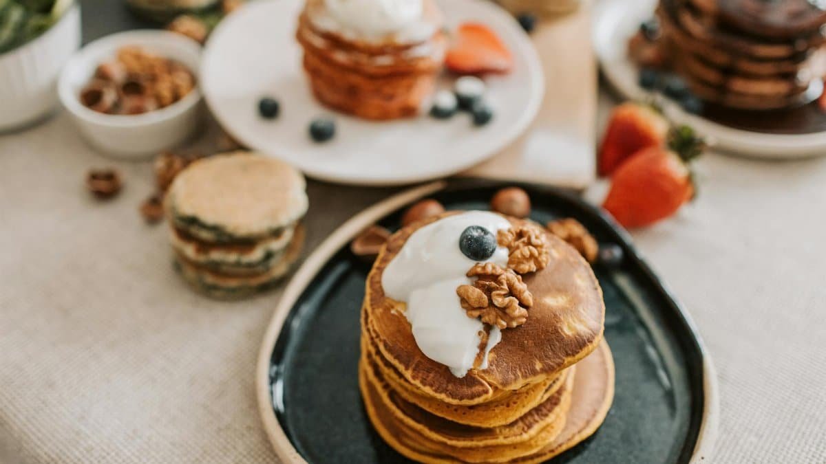 A stack of pancakes topped with yogurt, walnuts, and blueberries, perfect for a mouthwatering breakfast.