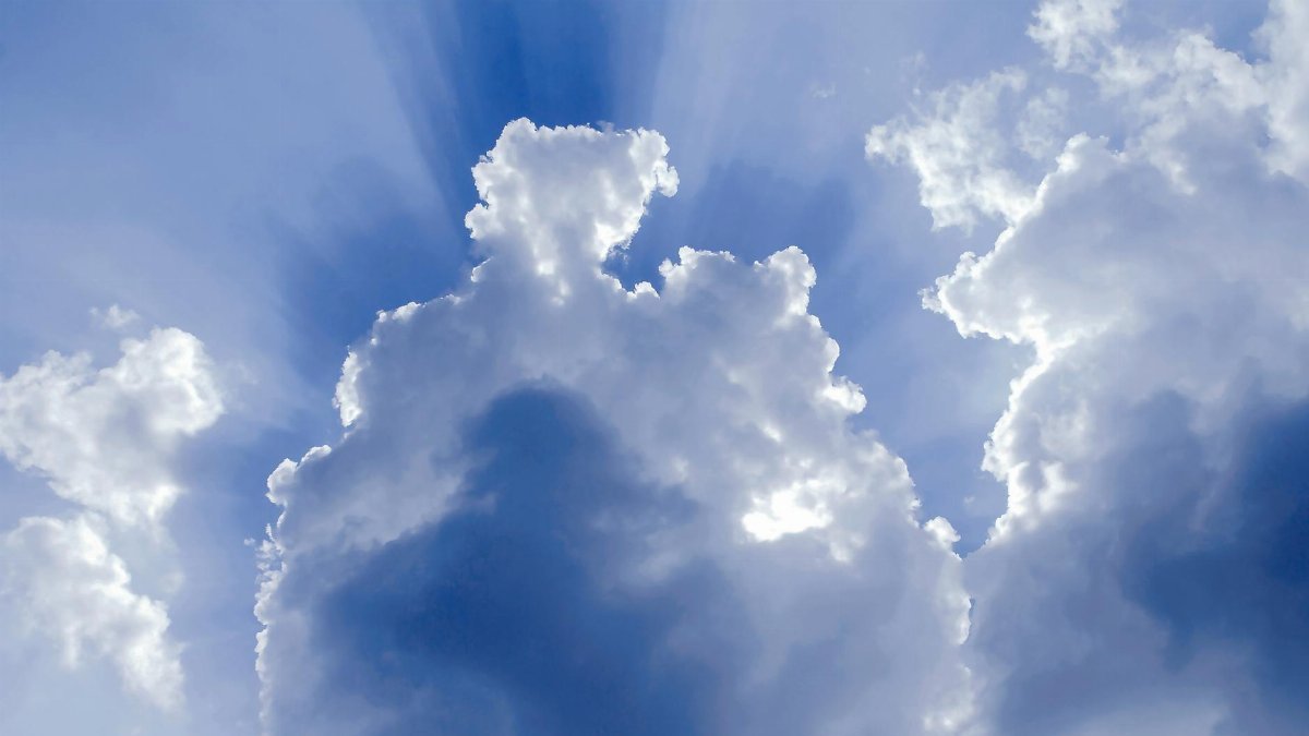 Dramatic cumulus clouds in a blue sky with sunlight streaming through, creating a stunning natural spectacle.
