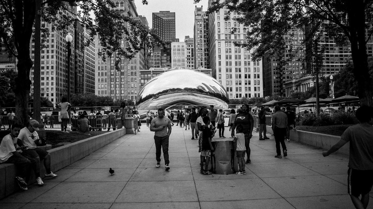 Monochrome scene of Chicago's Cloud Gate in Millennium Park with people and city skyline.