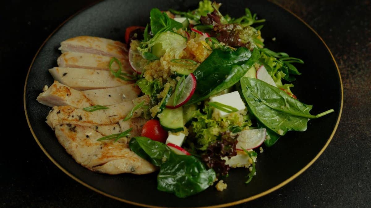 A vibrant salad featuring grilled chicken, quinoa, and fresh vegetables on a black plate.
