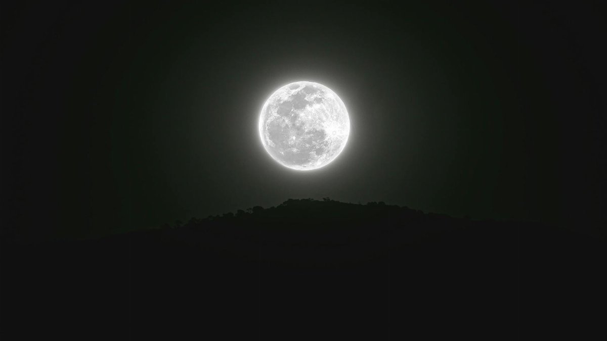 Stunning full moon illuminating the dark silhouette of Zapotitlán Salinas hills at night.