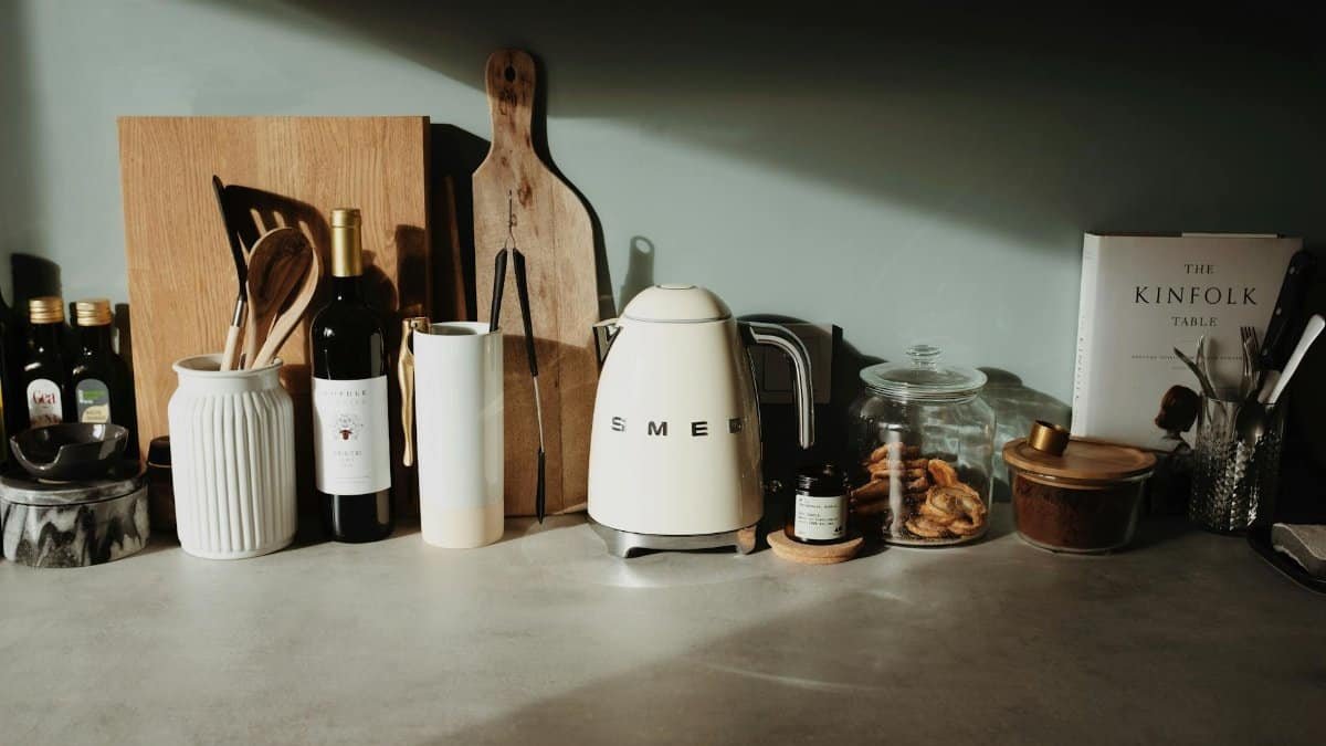 Various glass and ceramic bowls stylish electric kettle cutting boards and kitchen utensils locating on stone counter against gray wall in cozy kitchen