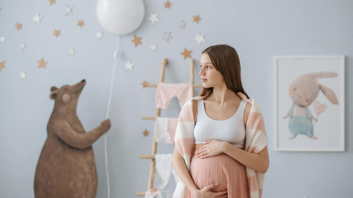 A beautiful pregnant woman in a stylish baby room, holding her belly.