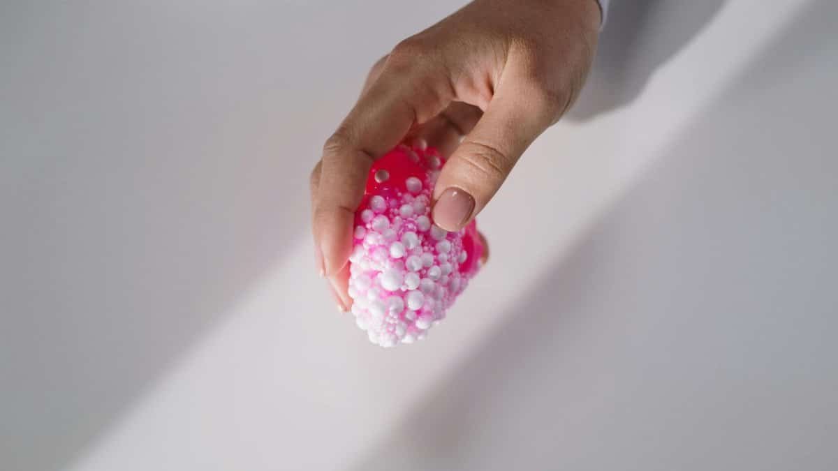 A hand gently holds a pink textured slime with small foam beads, showcasing tactile sensation.