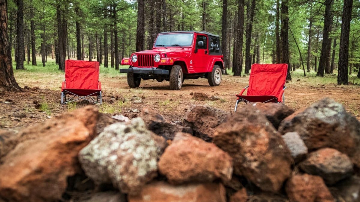 Scenic camping setup with red Jeep and chairs in Arizona's forested landscape.