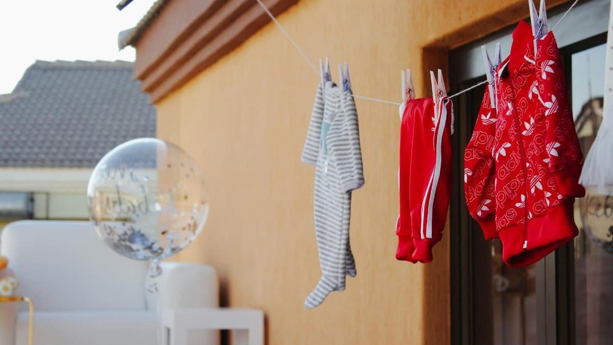 Baby clothes hanging on a clothesline next to a clear balloon against a wall.