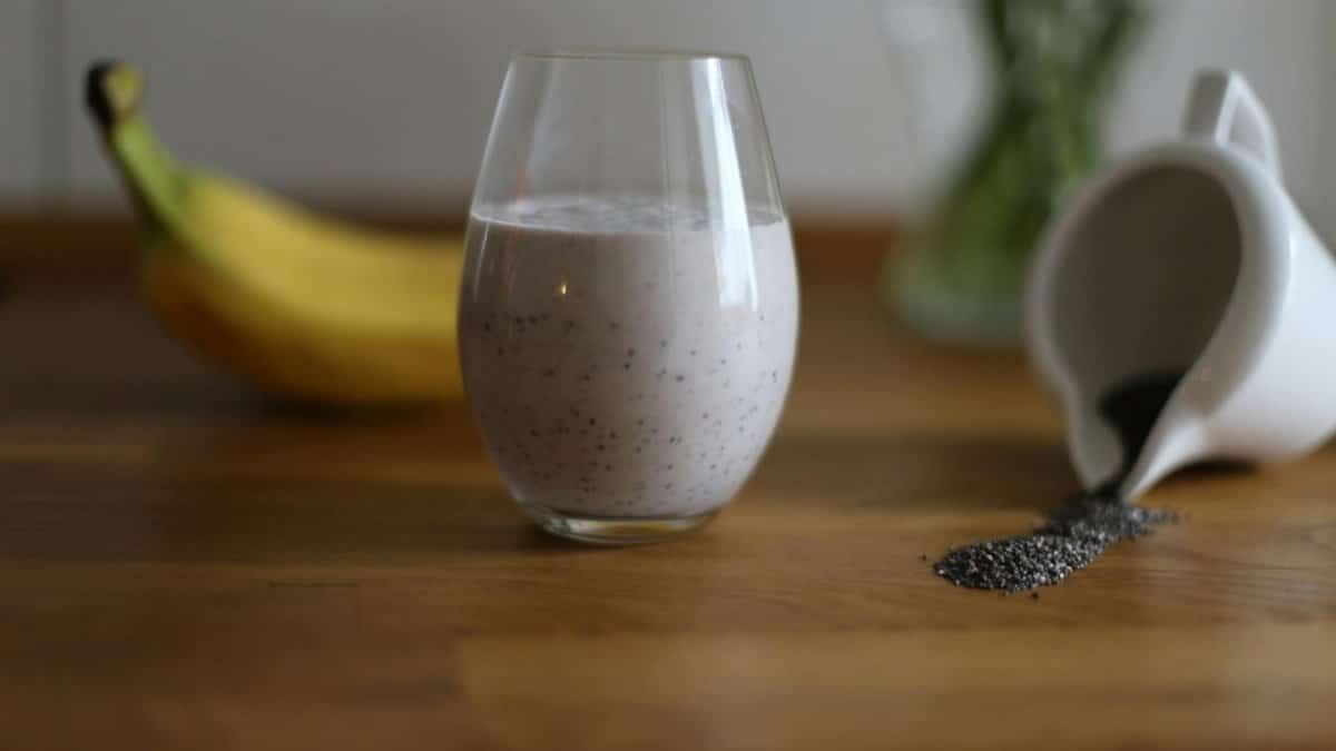 Glass of chia seed smoothie with banana and spilled seeds on wooden table.