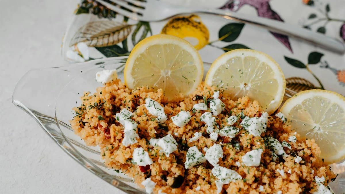 A vibrant dish of couscous with feta cheese, lemon slices, and herbs in a decorative setting.