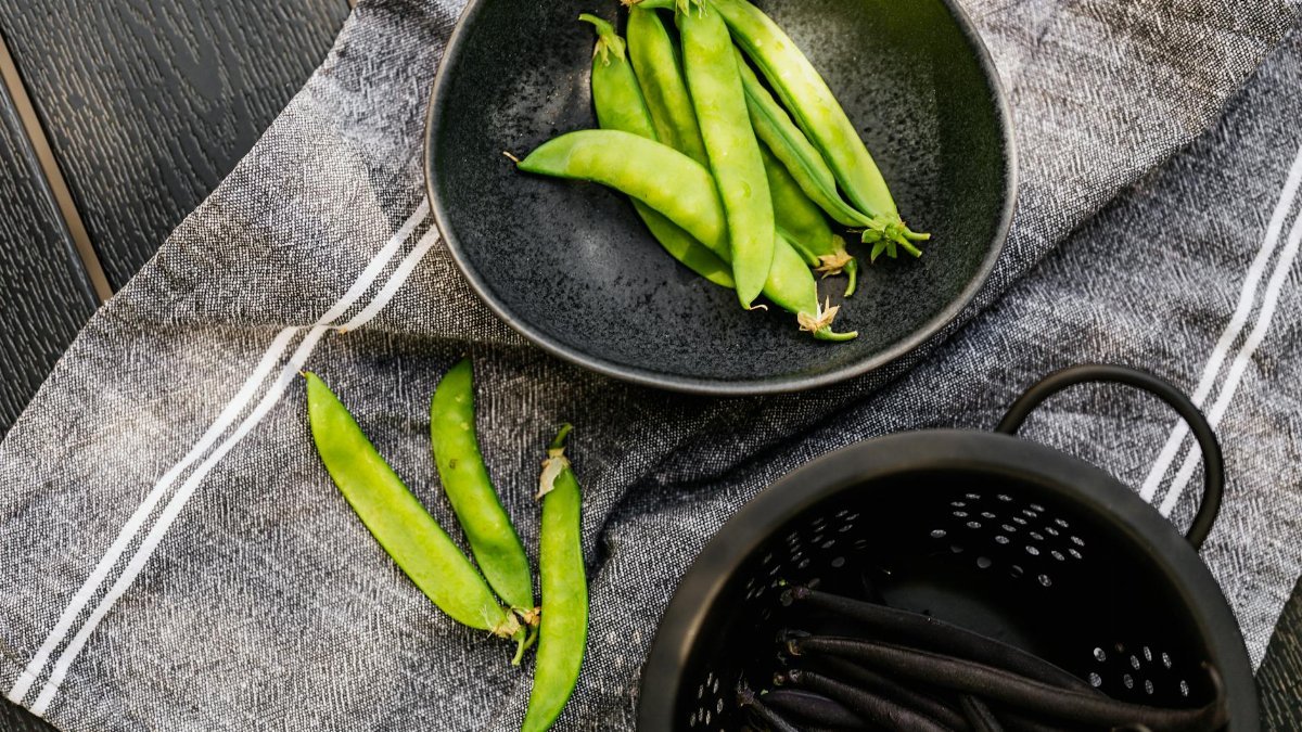 Close-up of fresh snow peas in a bowl and colander on a cloth background.
