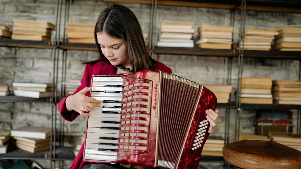 A young girl enjoys playing an accordion in a cozy library filled with books, showcasing her musical passion.