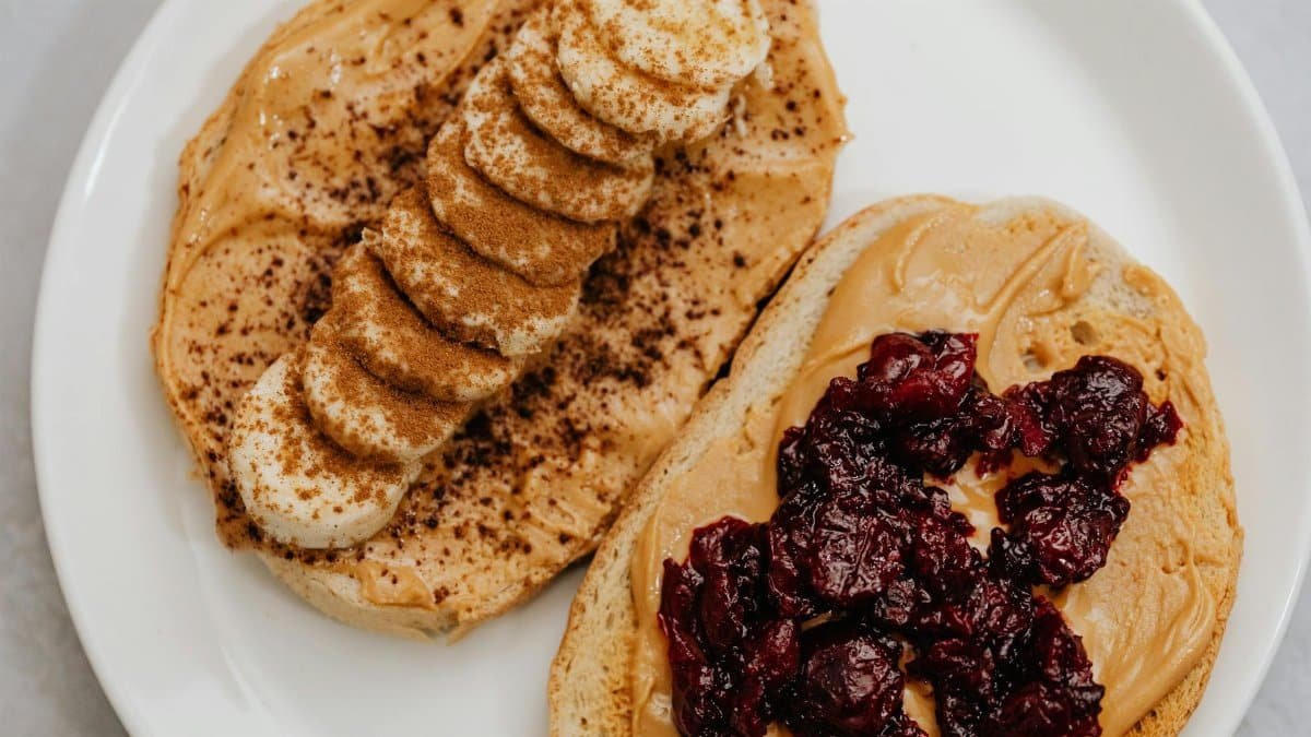Close-up of peanut butter toast with banana and jam toppings on a plate.