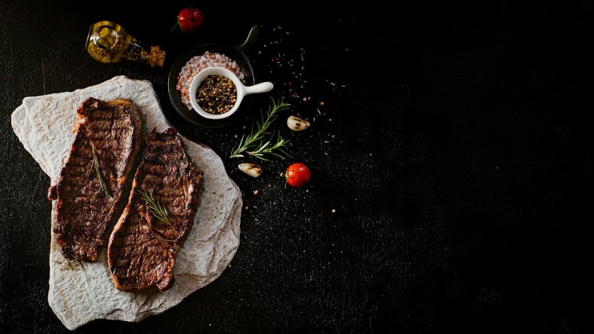 Delicious grilled steak served with rosemary, garlic, and spices on a stone slab, perfect for a gourmet meal.