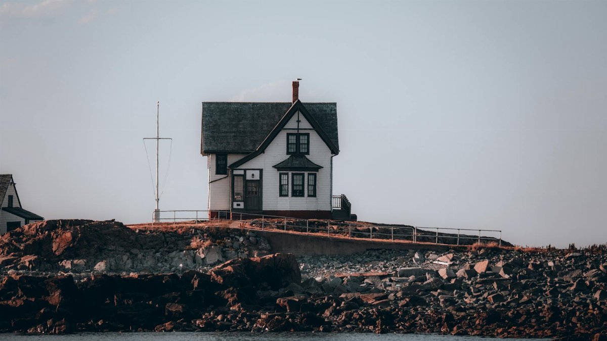 A picturesque lighthouse on a rocky coast under a clear sky in Boston, MA.