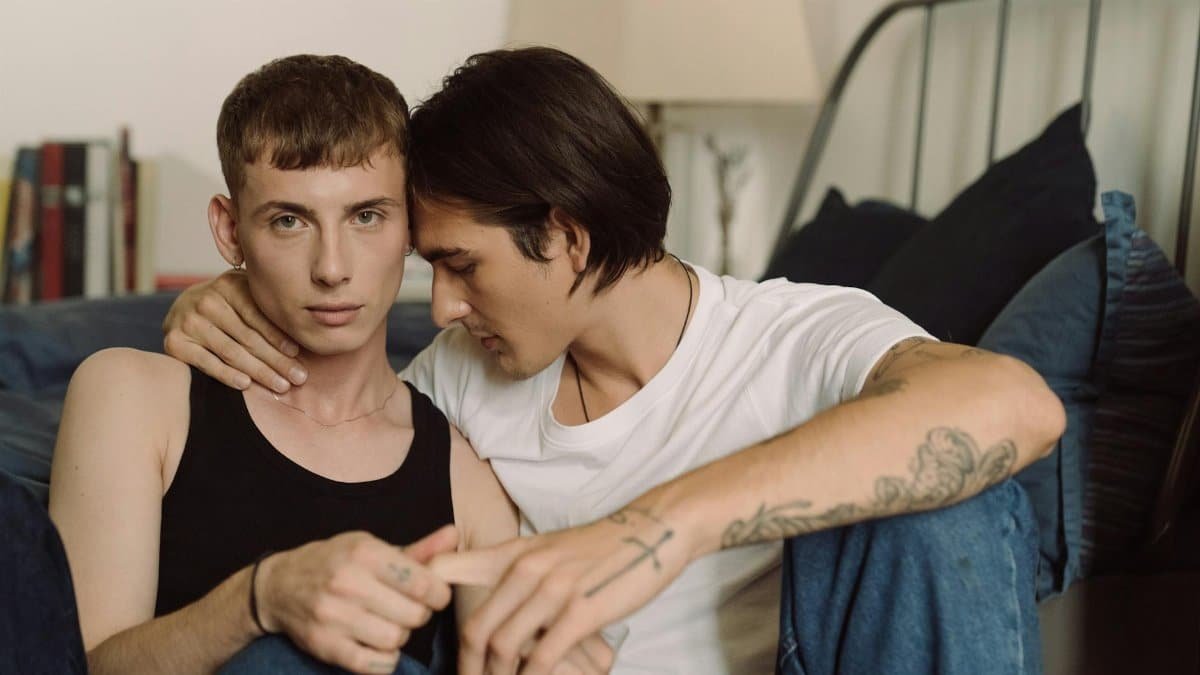 Two men sharing an affectionate and intimate moment indoors, embracing in a cozy setting.