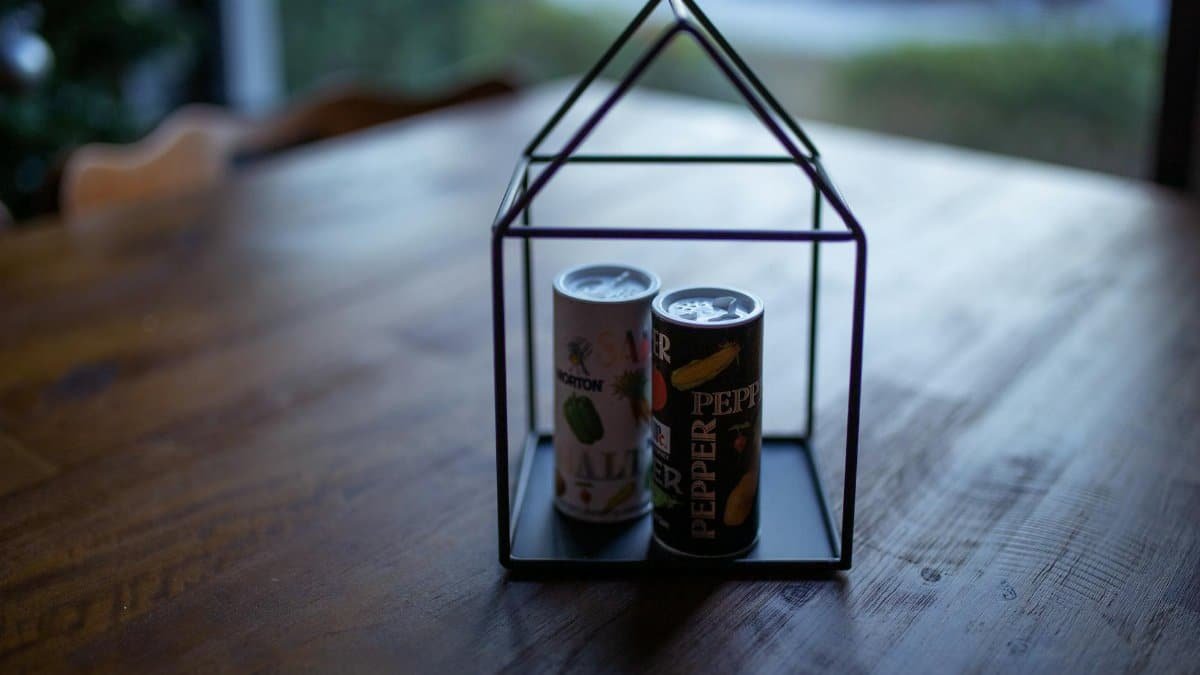 Artistic salt and pepper canisters in a geometric holder on a wooden table.
