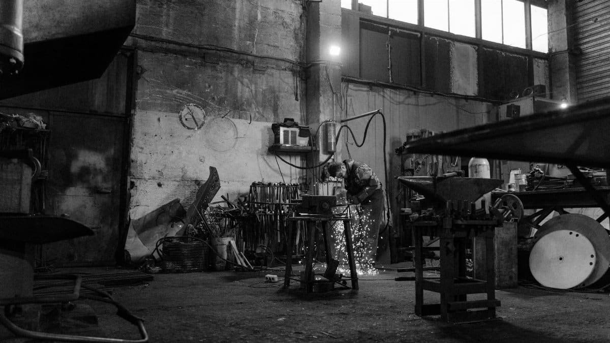 A blacksmith uses a grinder in a workshop producing sparks. Industrial setting.