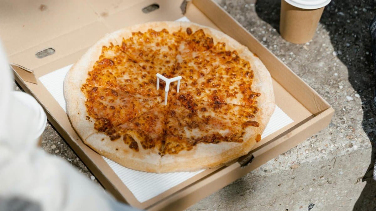 Cheesy pizza in an open box with a disposable cup, perfect for a casual outdoor meal.