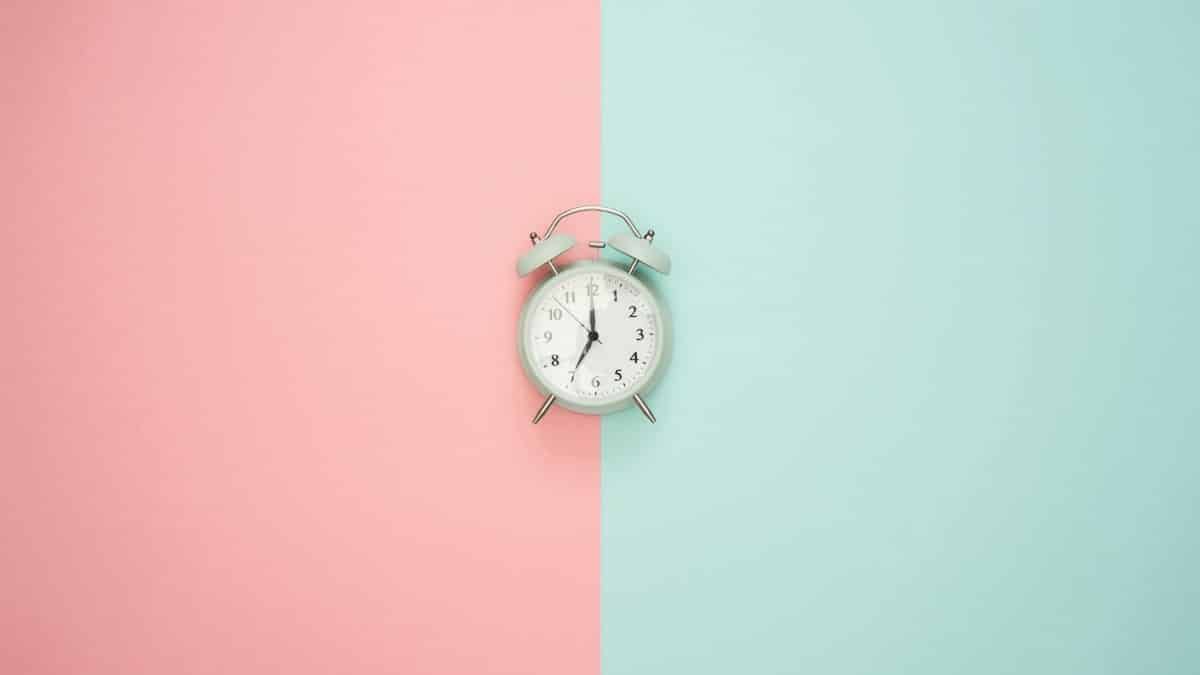 A vintage round clock on a split pastel pink and blue background.