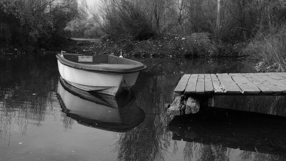 Serene black and white scene of a boat by a wooden dock in a still lake with reflection.