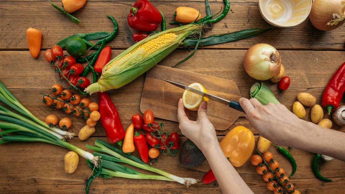 Top view of fresh vegetables and hands slicing a lemon on a wooden board.