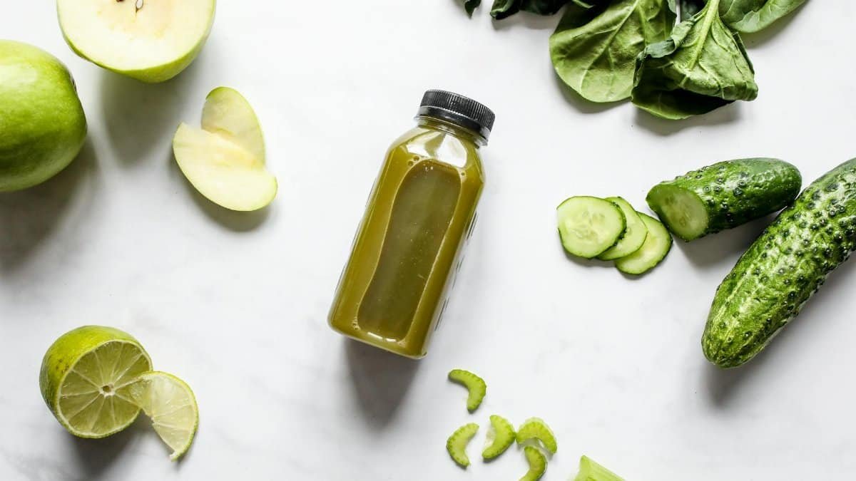 Discover fresh green juice surrounded by spinach, cucumber, apple, and lime.