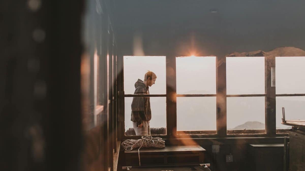 A man in a hoodie standing inside a mountain lookout with sunrise views in Ashford, WA.