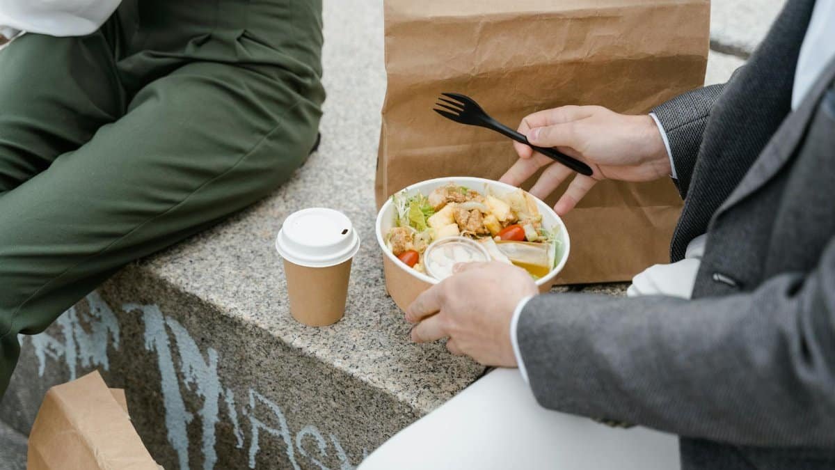 Two people enjoying a takeaway salad and coffee outdoors, seated on a stone bench.