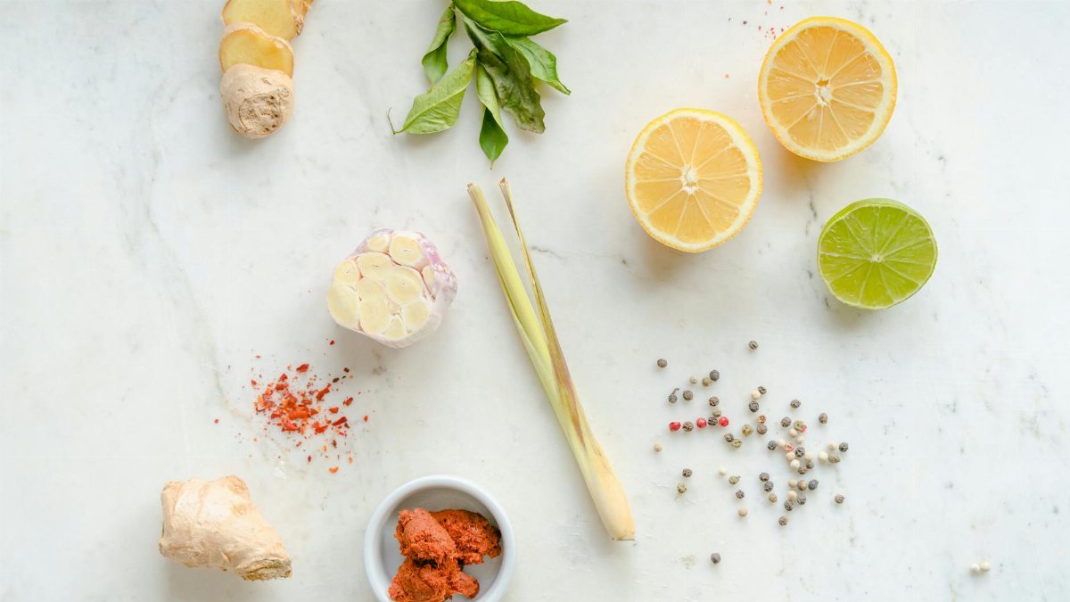 Top view of fresh ingredients including ginger, garlic, lemon, and spices on a white background.