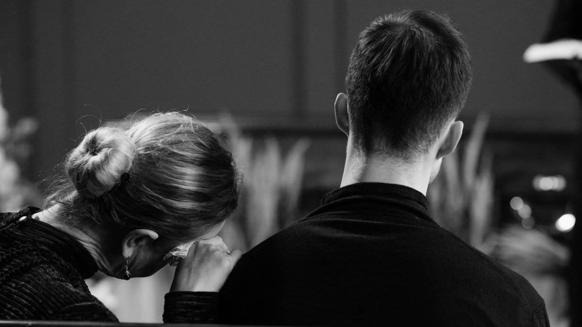 A couple sitting indoors, captured in grayscale, showing shared sorrow and loss.