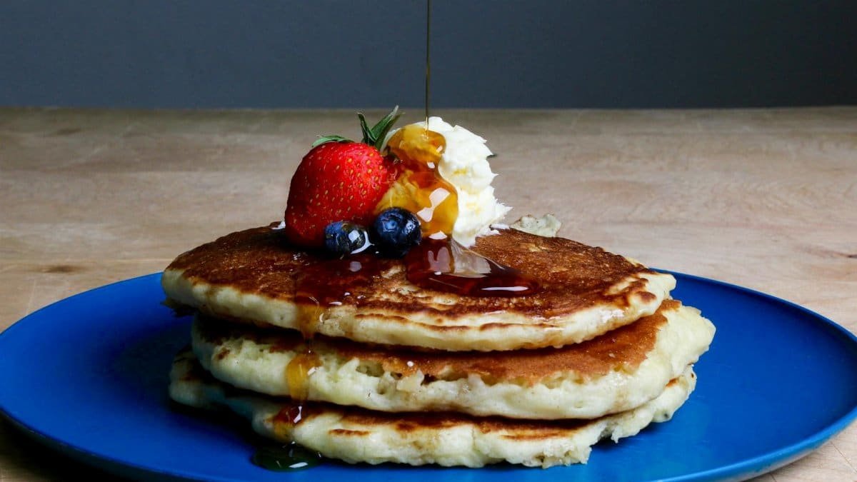 Stack of fluffy pancakes topped with syrup, strawberries, blueberries, and cream on a blue plate.