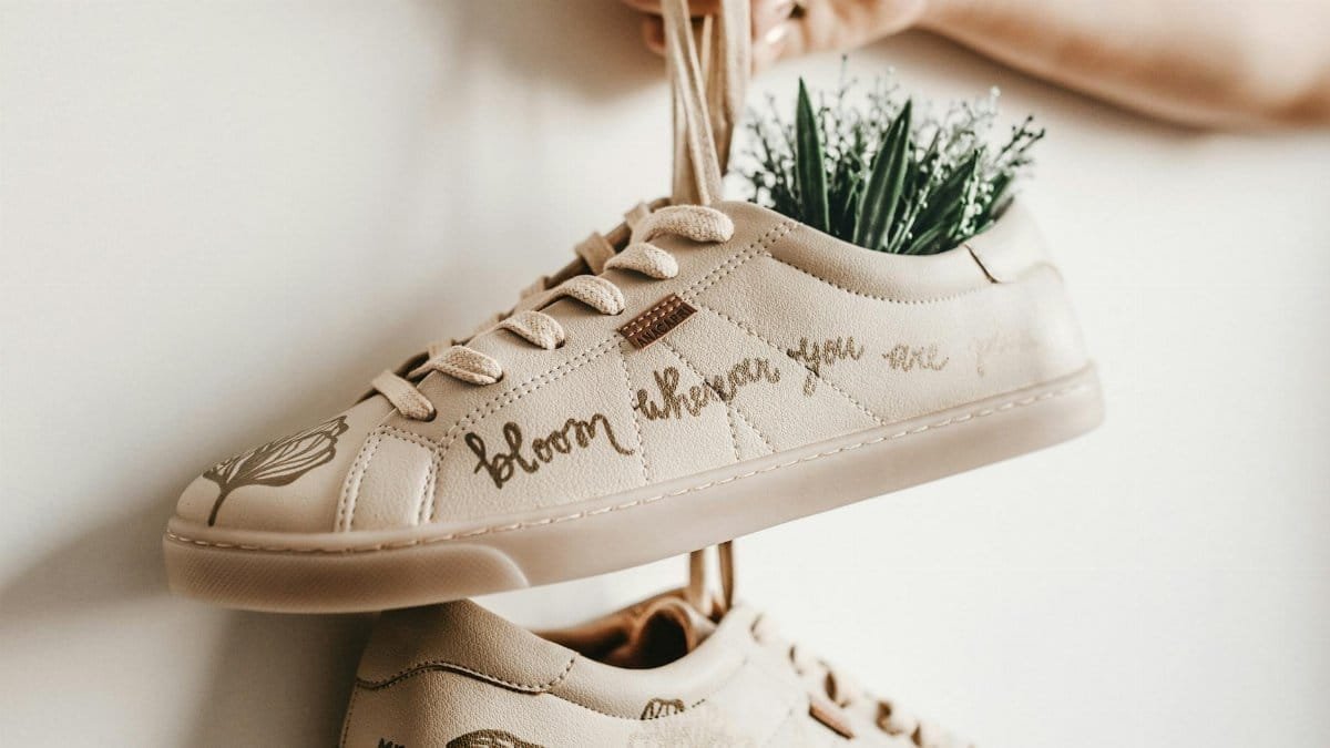 Close-up of beige sneakers with plant design and 'bloom where you are planted' script.