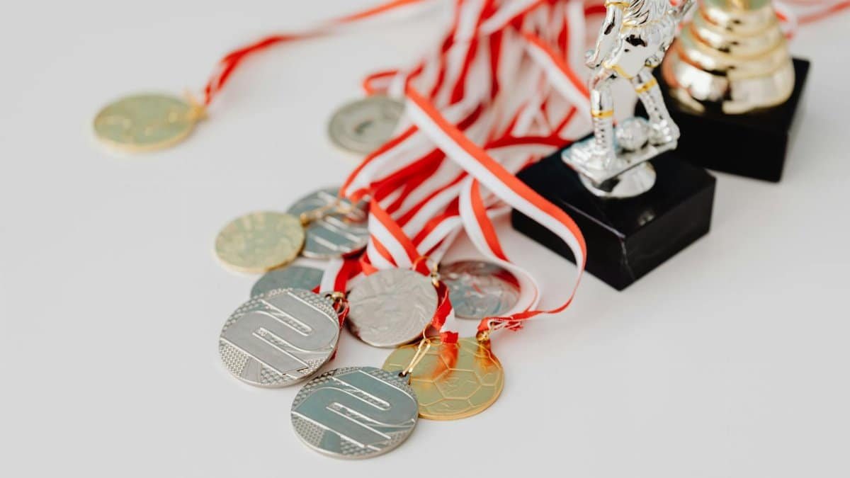 A varied collection of silver and gold medals alongside trophies on a white surface, showcasing achievement.