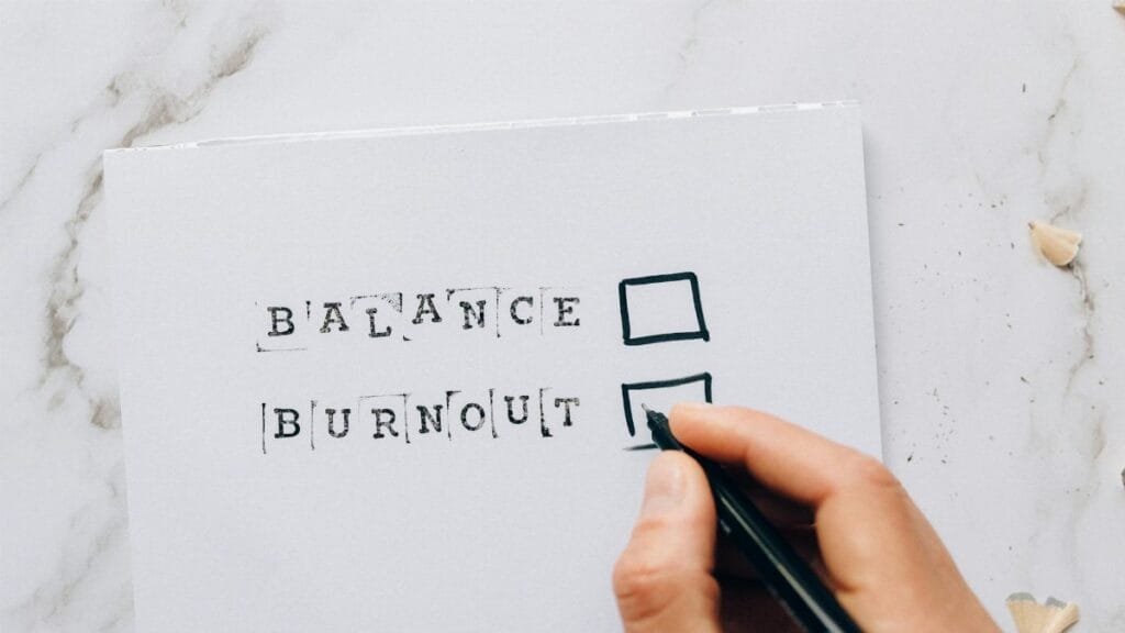 Close-up of a hand hovering over a checklist with options for balance or burnout, symbolizing stress and choice.