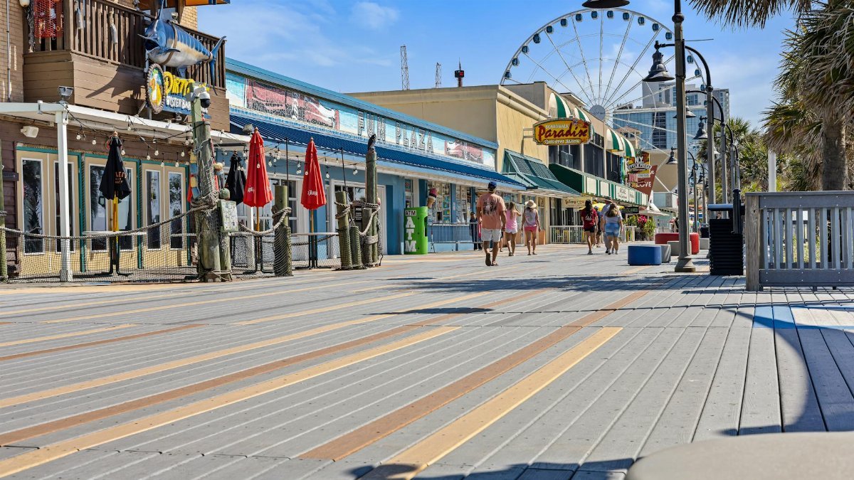 Explore the lively Myrtle Beach boardwalk with shops, a Ferris wheel, and visitors in the summer sunshine.