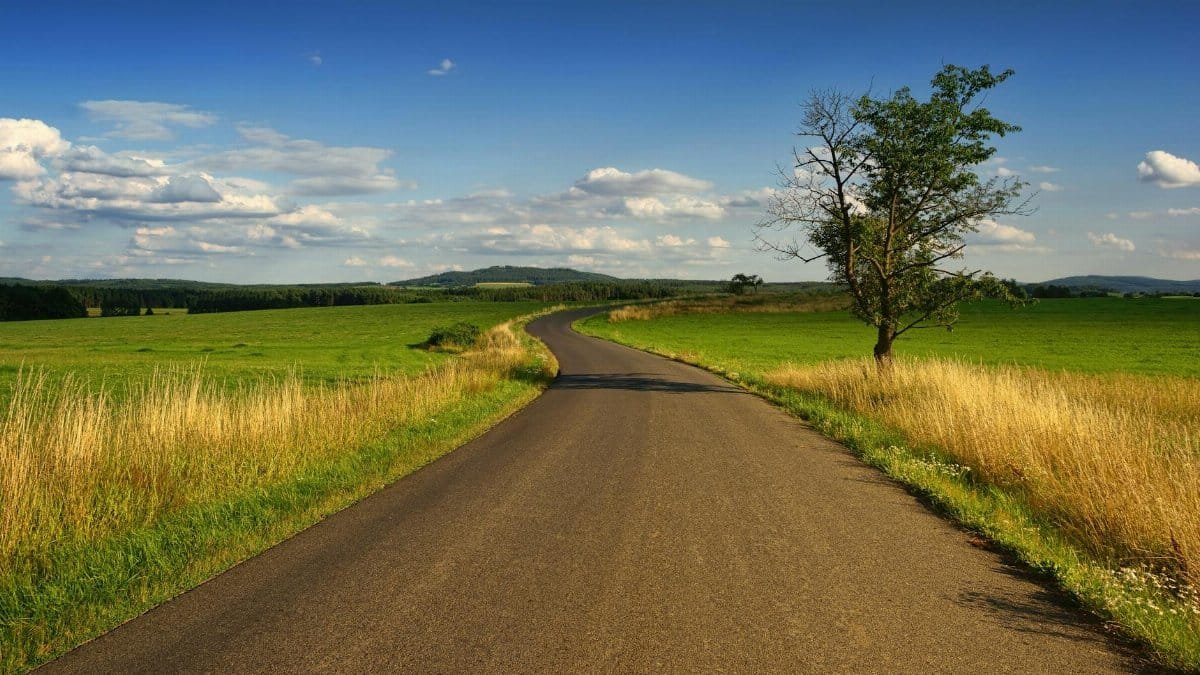 Scenic view of a winding road through peaceful countryside fields with blue skies.