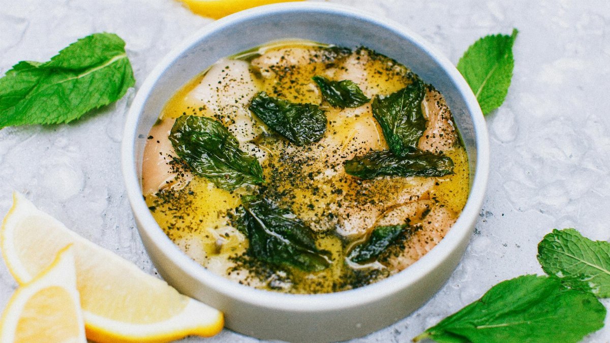 A close-up of a delicious lemon and herb fish soup garnished with fresh mint leaves, perfect for a refreshing meal.