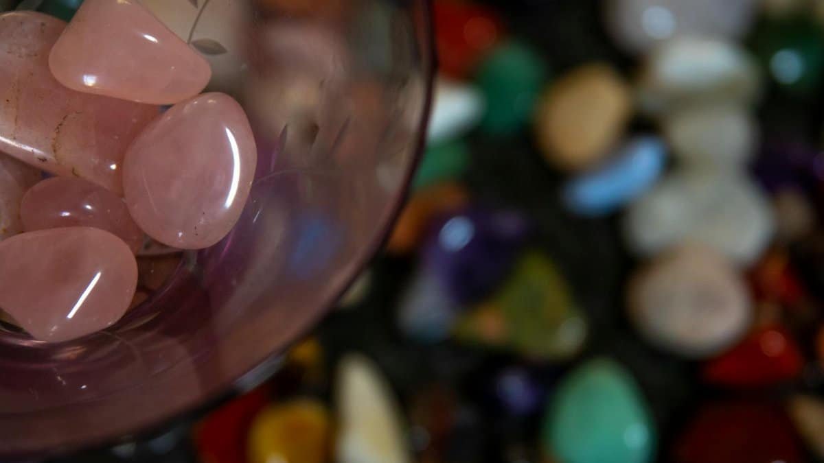 Close-up of rose quartz stones in glass with a blurred background of various colorful pebbles.