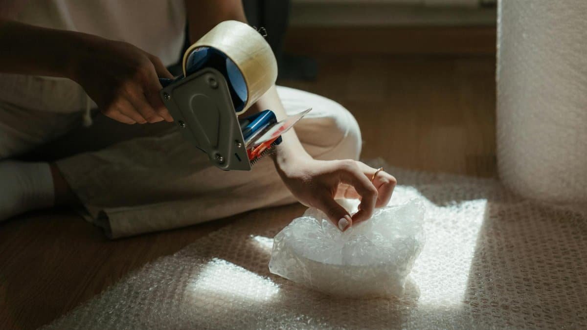 Close-up of a person preparing a package using bubble wrap and tape, indoors.