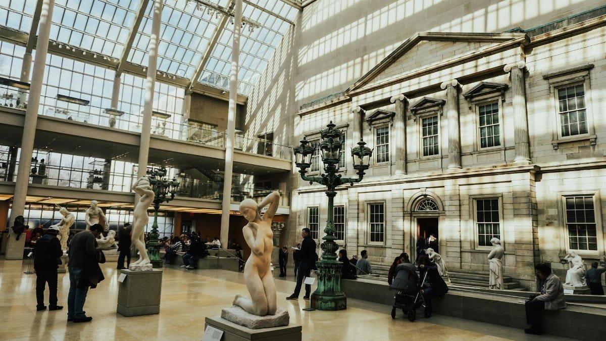 Sunlit atrium with statues and visitors at the Metropolitan Museum of Art, New York.