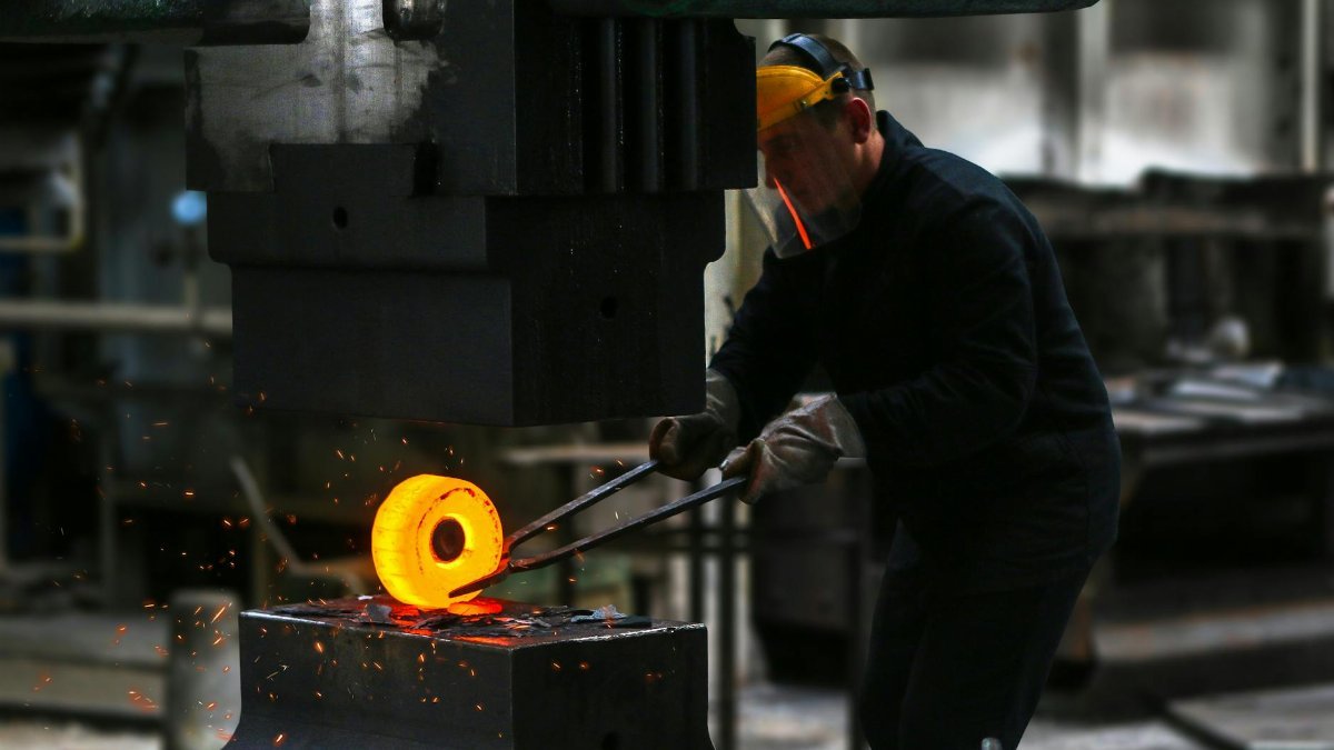 A blacksmith skillfully working with red-hot metal in an industrial setting, showcasing craftsmanship.
