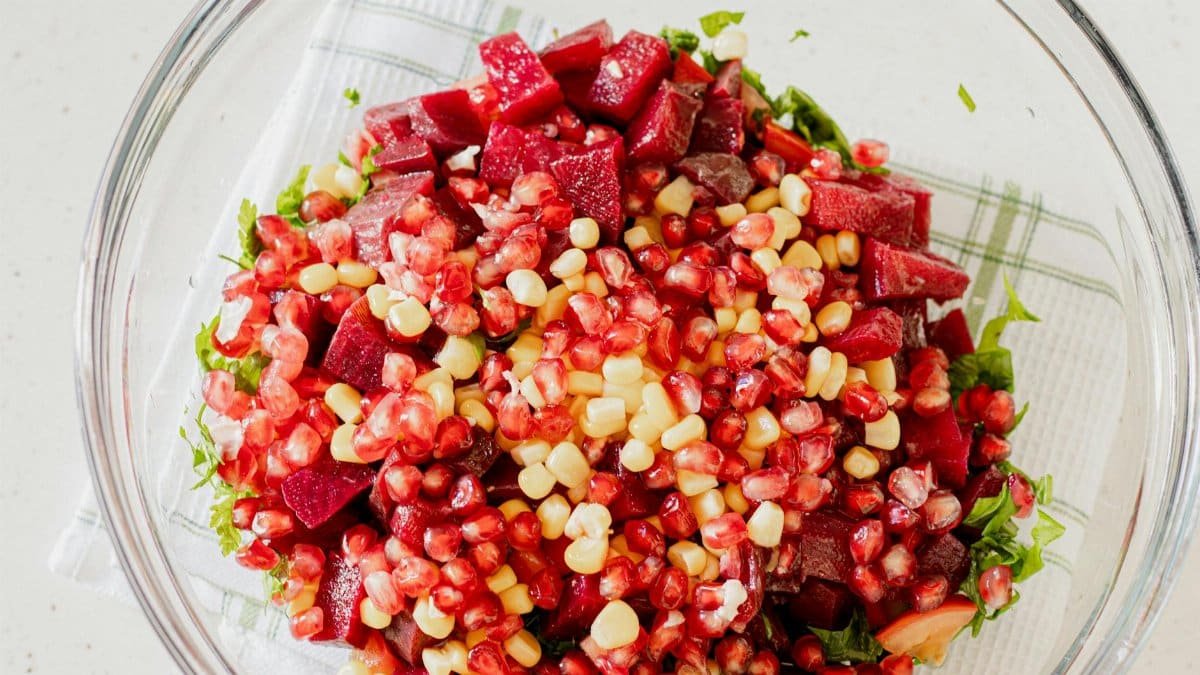 Colorful salad with pomegranate, corn, and beets in a glass bowl.