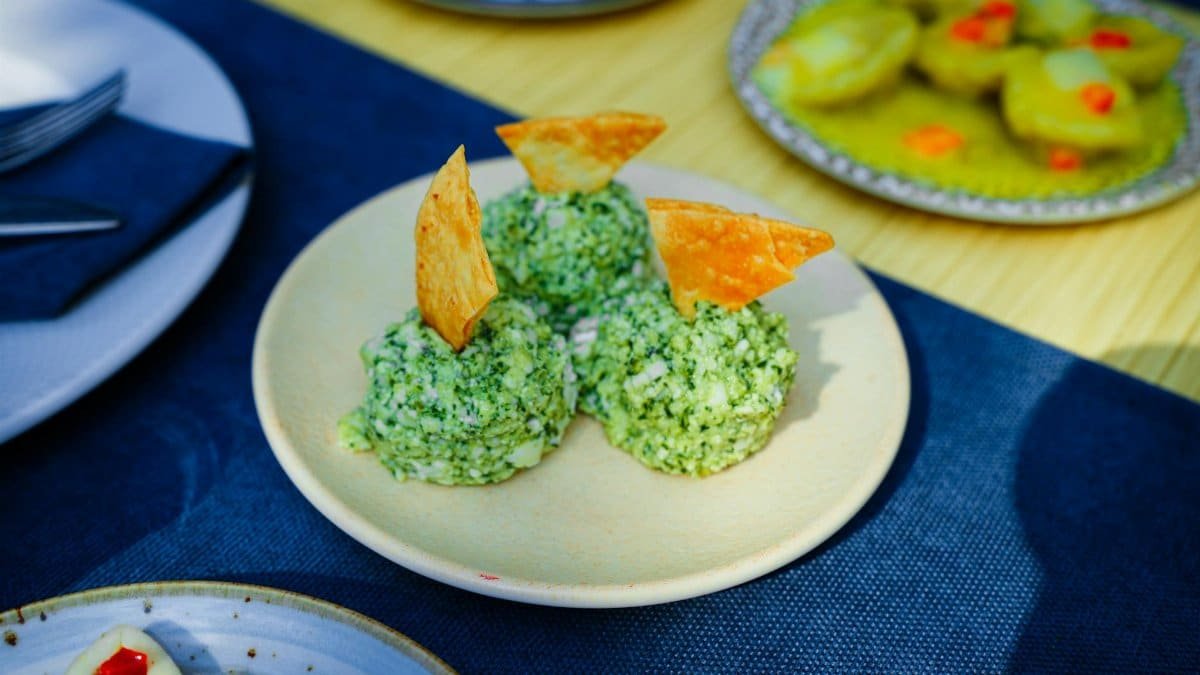 Plate of green cheese balls garnished with crispy chips on an outdoor table.