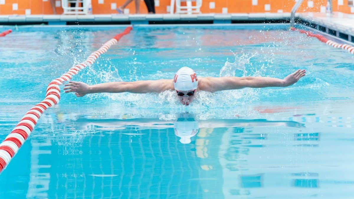 Athlete in a swimming pool executing a powerful butterfly stroke, creating dynamic water splashes.
