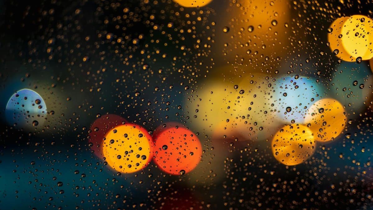 Raindrops on window with vibrant bokeh lights creating an abstract nighttime view.