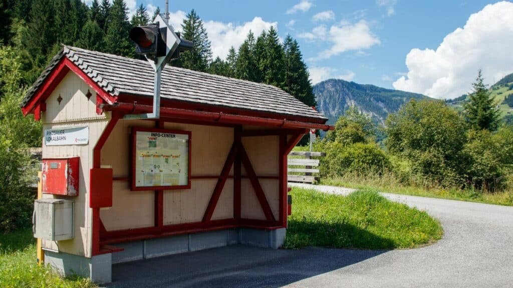 An idyllic alpine bus stop surrounded by lush greenery and mountains on a sunny day.