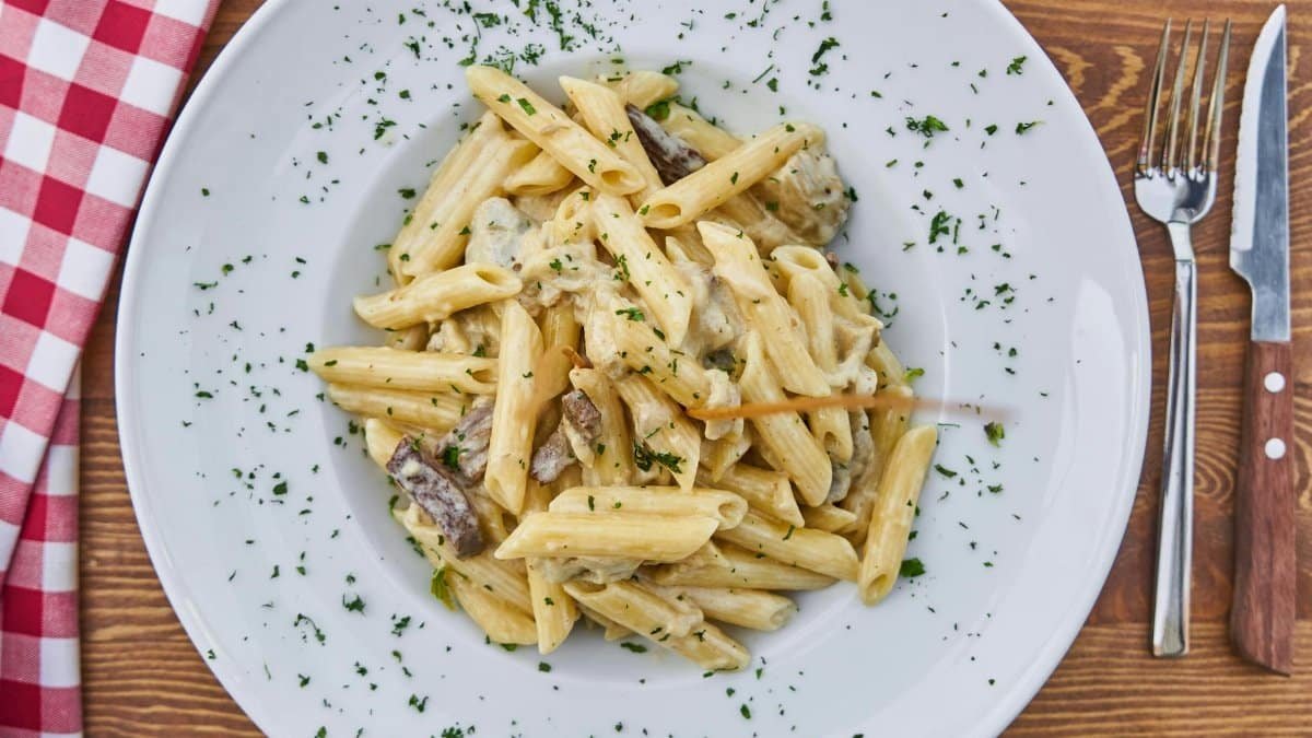Delicious creamy penne pasta with mushrooms and parsley on a rustic table setting.